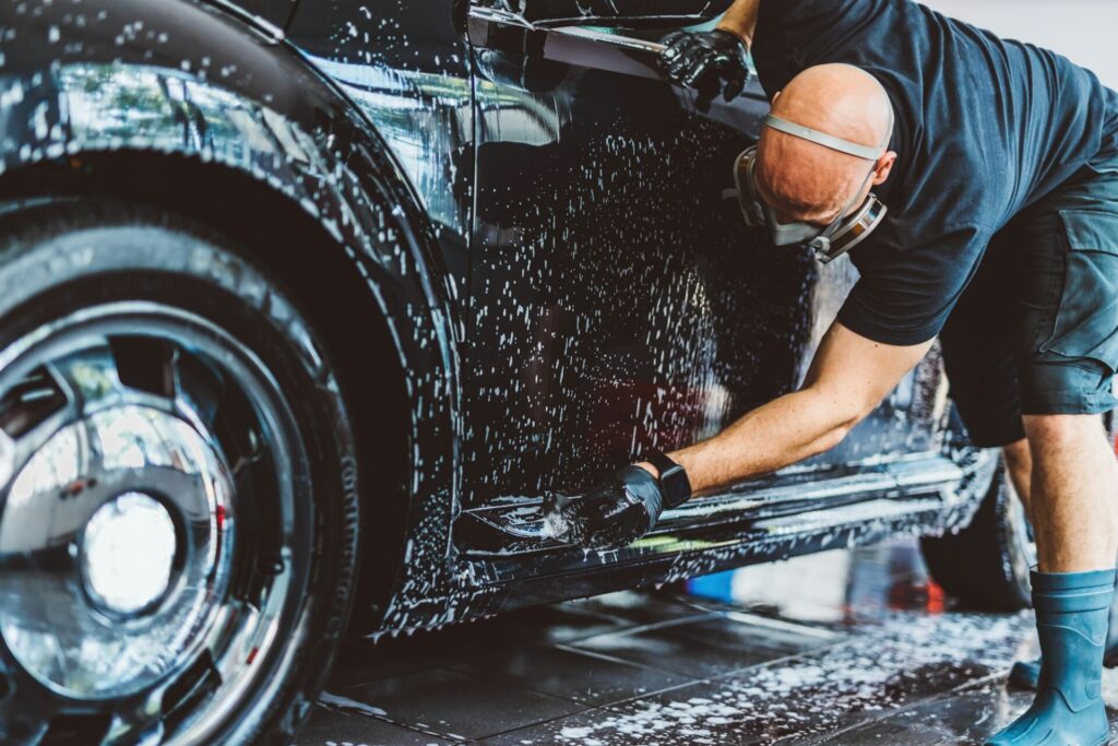 Service man washing car before detailing in workshop.